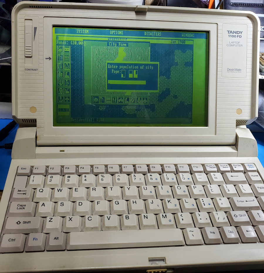 Tandy 1100FD displaying the SimCity gameplay screen in monochrome green/black. The copy protection dialog is on top.