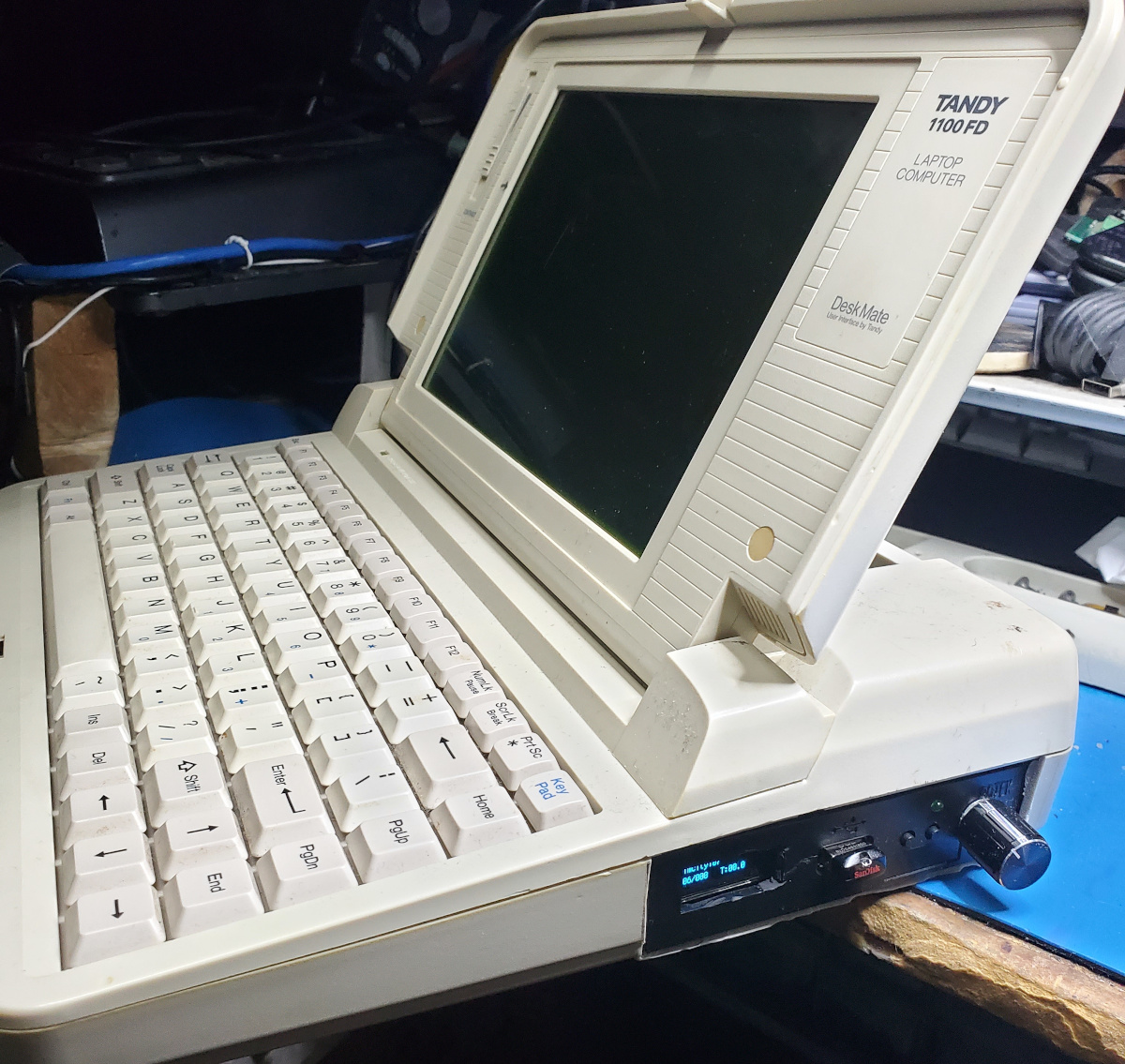 Side view of the Tandy 1100FD, with the screen in the upright position. A Gotek floppy emulator with LCD and jog dial mods is installed in the side where the floppy drive used to be.