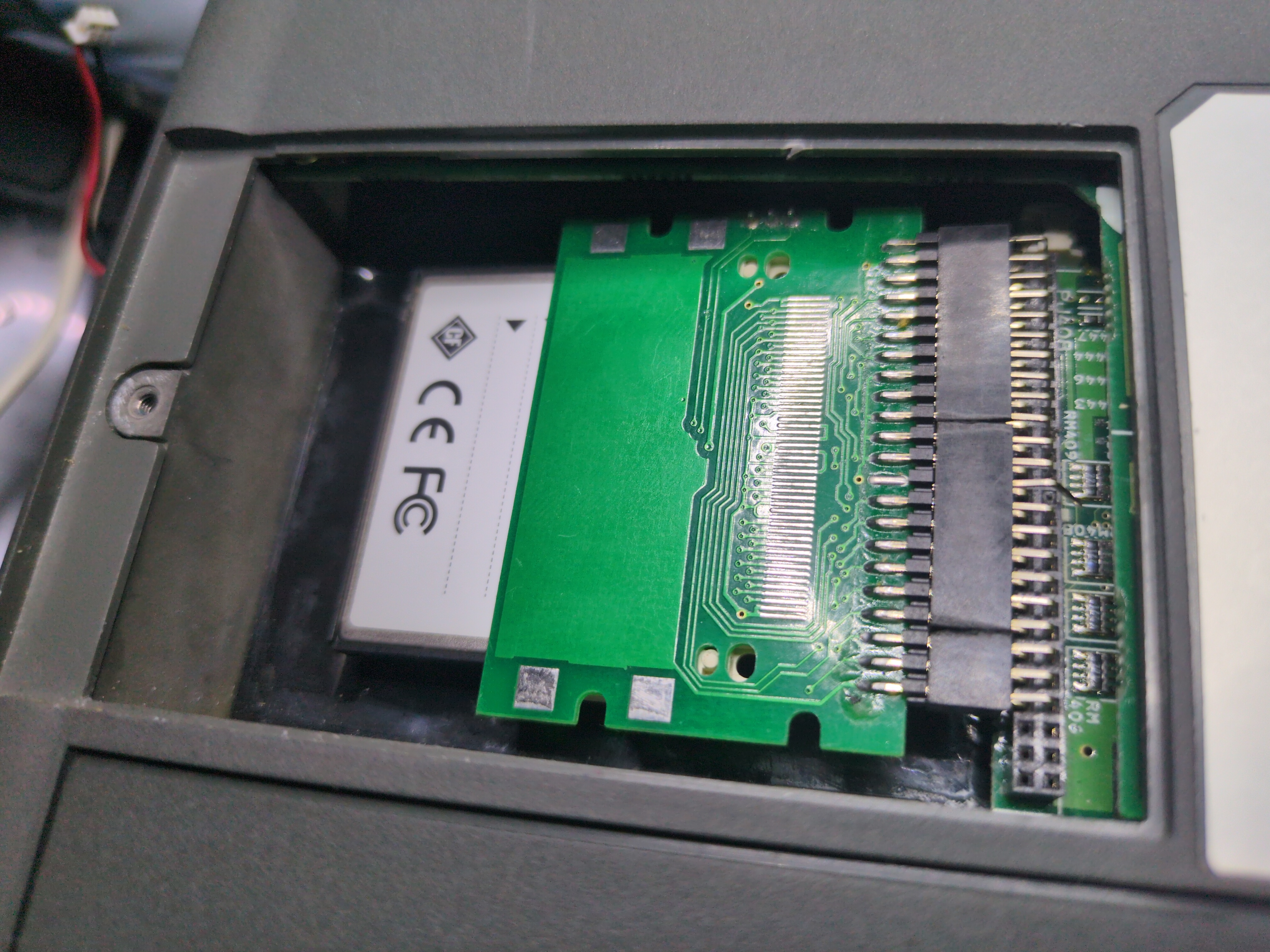 Photograph of the back compartment of the T200 tablet computer. The service panel is removed exposing a Compact Flash card in an adapter attached to the IDE connector with multiple angled multi-row pin extenders.