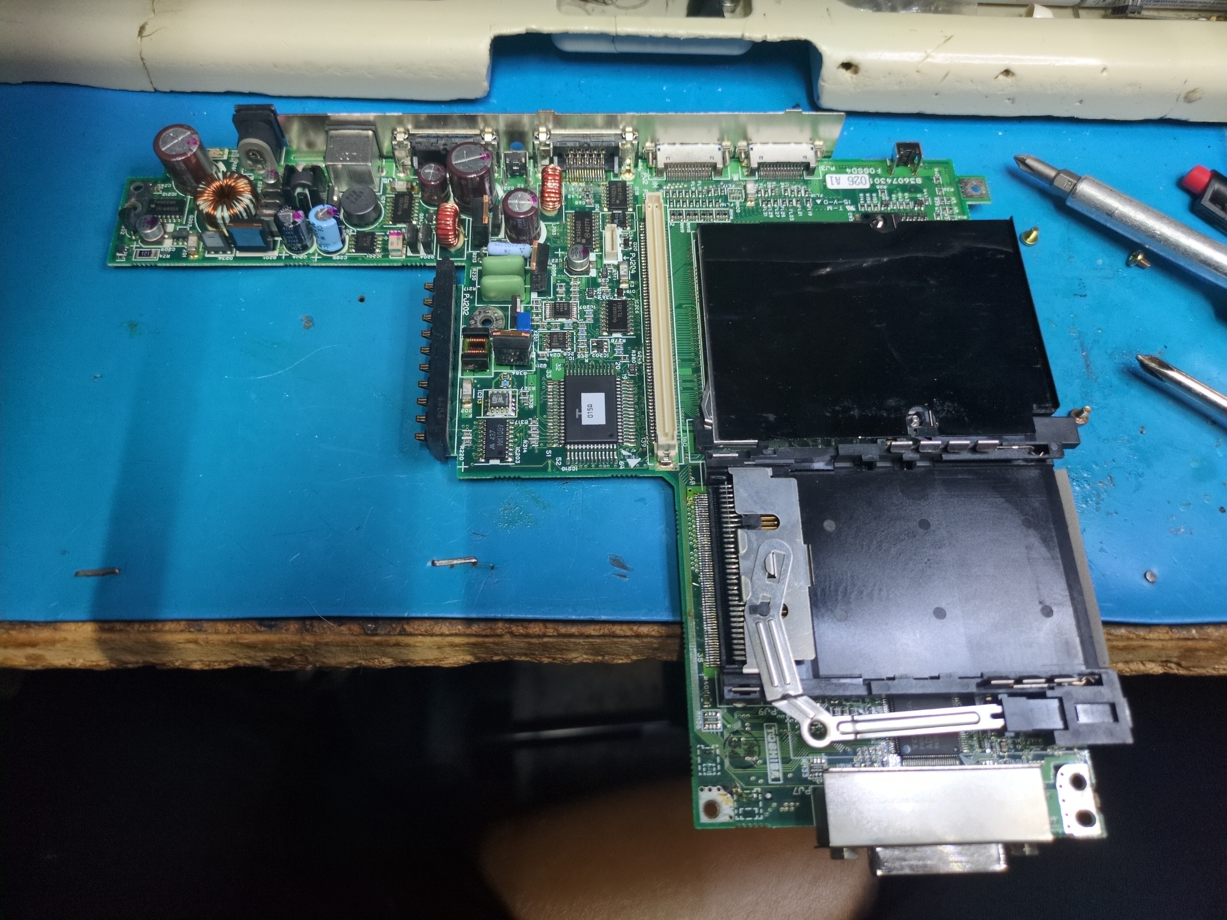 Photograph of a computer circuit board. Large plastic sheets conceal the PCMCIA card slots and a variety of large passive components assumed to be part of the power supply occupy the upper-left portion of the board. A linear connector in the middle connects it to the display board above.