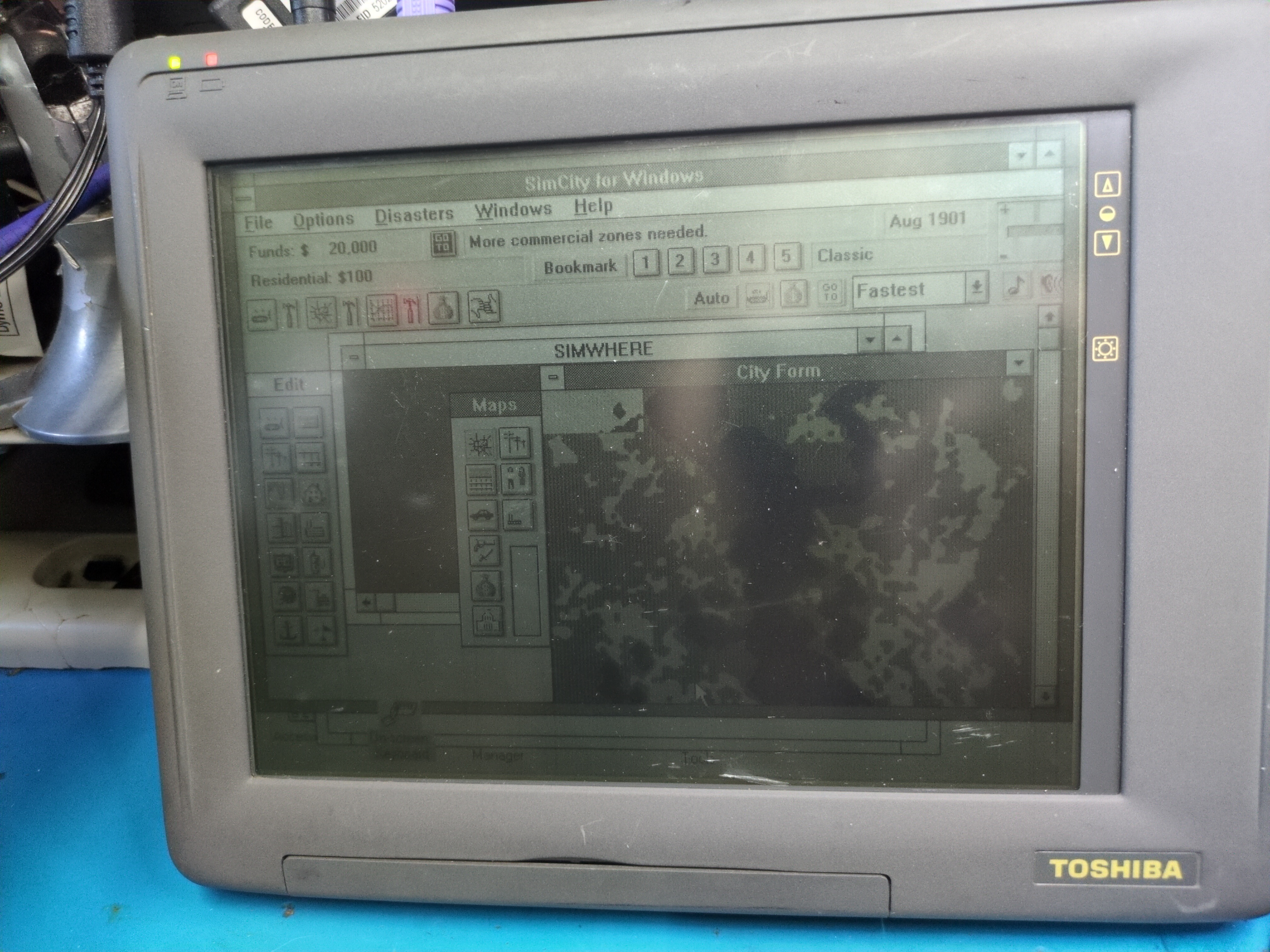 Photograph of a Toshiba tablet computer. The screen backlight is off but it's an old-timey reflective monochrome LCD so SimCity for Windows is still visible running on the computer.