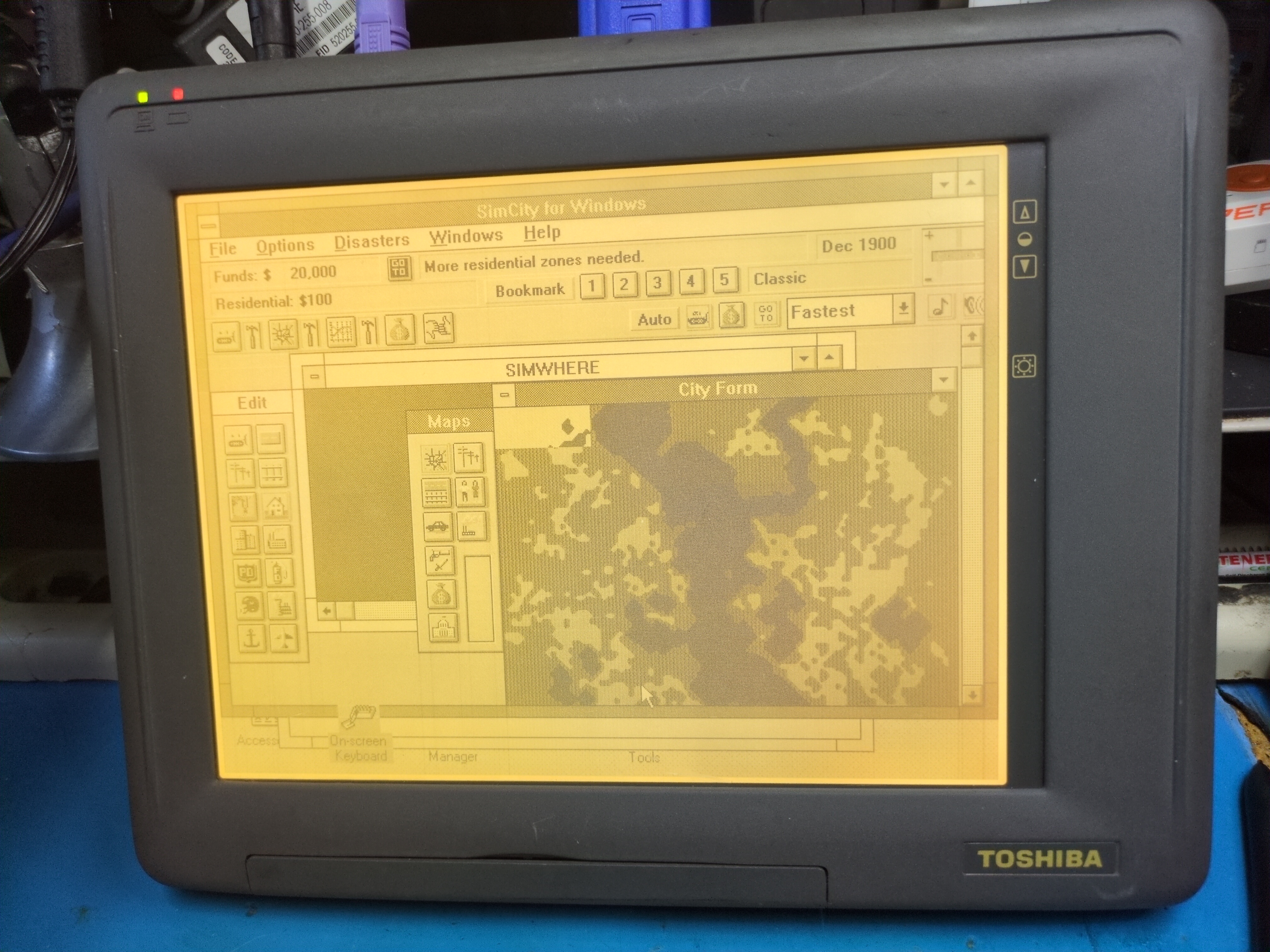 Photograph of a Toshiba tablet computer. The screen backlight is on and SimCity for Windows is visible running on the computer.